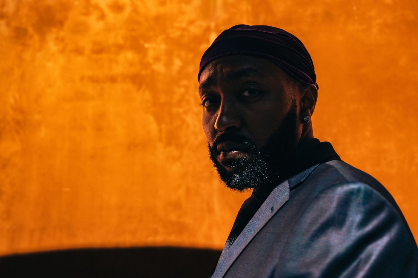 Menasseh in a suit against an orange wall